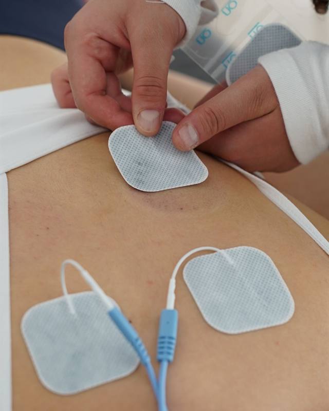 Fisioterapeuta colocando electrodos en la espalda de un paciente